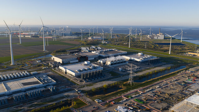 Aerial view of the Google data center complex surrounded by numerous wind turbines and industrial infrastructure under a clear sky in Eemshaven, Groningen, Netherlands.