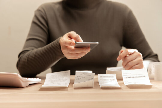 Women using smartphone calculate paper receipts on table. Calculating bills, expense tracking, personal finance