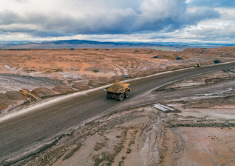 Aerial view shows large dump truck transporting materials on a wide dirt road at an open pit mine site during daytime © Evgenii Bakhchev