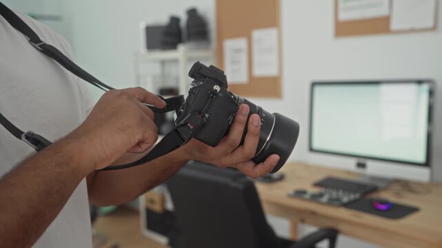 Man holding camera, fingers adjusting lens and pressing shutter button in studio; quiet concentration.