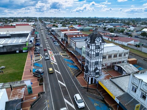 Aerial view of Stratfords main street, showcasing the iconic clock tower and the town's layout. Cars drive along the road, and people walk on the sidewalks in New Zealand.