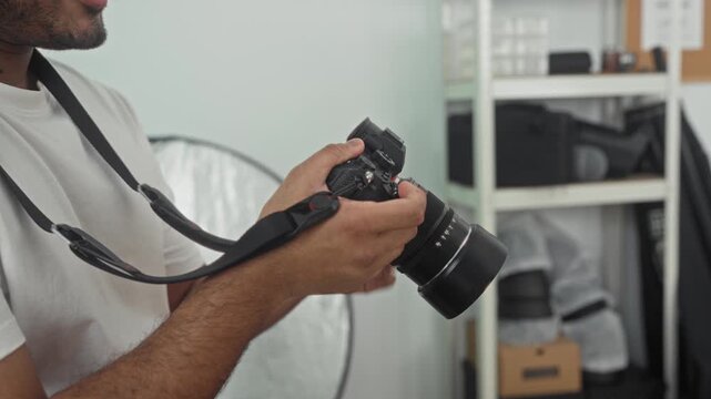 Young man photographer holding camera with both hands and adjusting lens in studio; concentration precision.