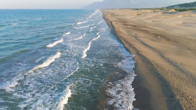 Gelemis, Turkey. Vast Patara Beach with tiny man walking, endless coastline to horizon, morning light and waves. Aerial View, Departure of the camera