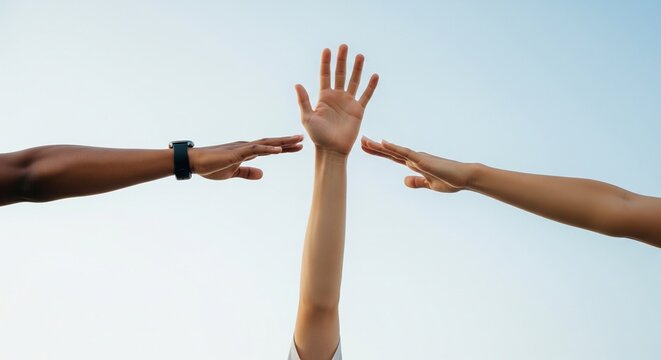 Diverse hands reaching up together against a clear blue sky symbolizing unity and teamwork
