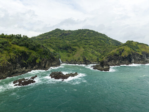 Aerial view of Banyutibo Water Fall cascading from lush green cliffs into the turquoise ocean waves in Girisubo, Special Region of Yogyakarta, Indonesia.
