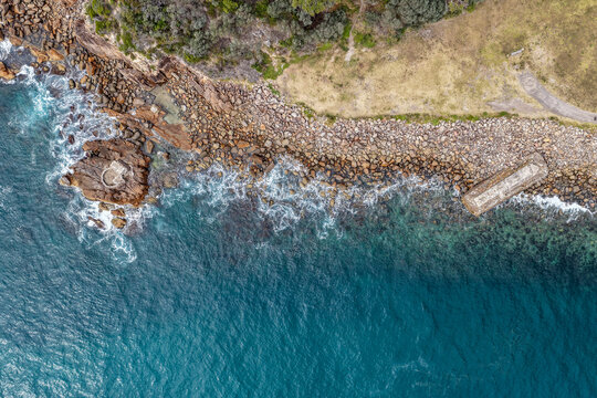 Aerial view of World War II torpedo and gun emplacement at Tomaree Head in New South Wales, Australia surrounded by rugged rocky coastline and turquoise ocean. 