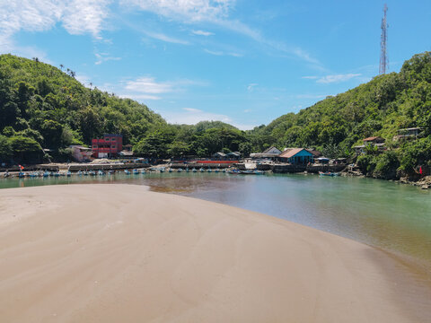 Aerial view of Baron Beach featuring traditional fishing boats moored along the river mouth, surrounded by lush green hills and a sandy shoreline Tanjungsari, Special Region of Yogyakarta, Indonesia.