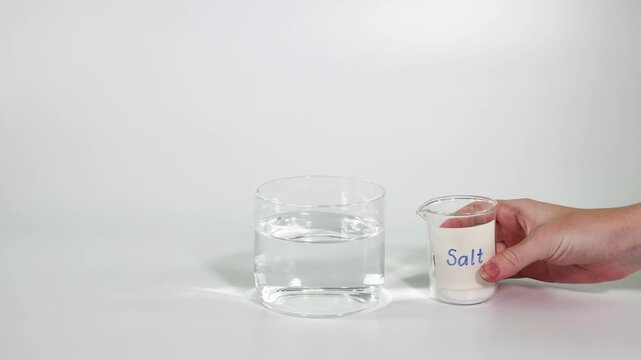 Pouring salt from a beaker into a glass of clear water for a science experiment.