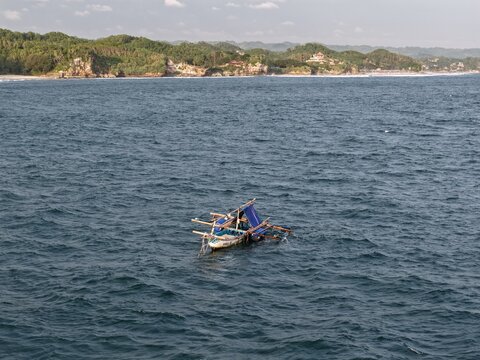 Aerial view of a traditional fishing boat on the blue sea near the green cliffs of Baron Beach in Tanjungsari, Special Region of Yogyakarta, Indonesia.