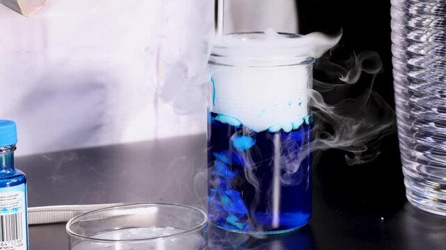 Chemical reaction with dry ice in blue liquid creating dense white vapor inside glass jar.