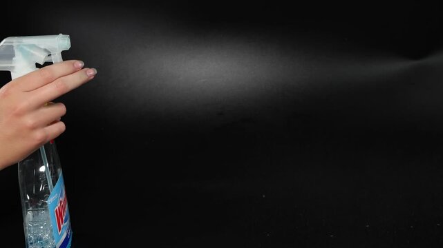 Spray bottle nozzle spraying mist in slow motion against black background.