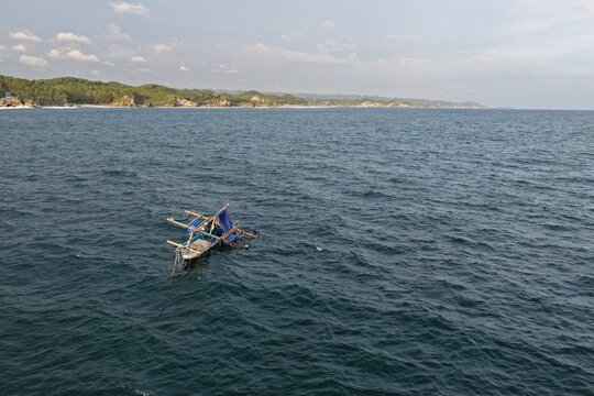 Aerial view of a traditional fishing boat floating on the deep blue sea near the coastline of Baron Beach in Tanjungsari, Special Region of Yogyakarta, Indonesia.