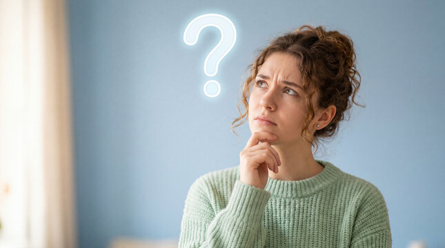 Confused young woman with hand on chin looking up at a glowing neon question mark icon above her head against a blue wall background thinking about a problem or making a difficult decision
