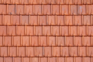 Fototapeta premium close-up photograph displays a uniform pattern of burnt orange, terracotta-style roof tiles. The tiles are interlocking, with rounded upper parts and decorative lines.