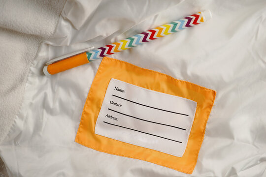 A label with lines for name, contact, and address on child fabric with a pen