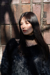 Fototapeta premium 木漏れ日が顔に差す、冬の装いの女性。屋外でのファッションポートレート