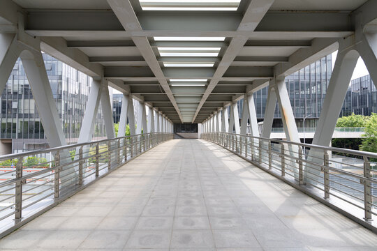 Empty modern pedestrian skybridge with white steel arch structure and symmetrical perspective