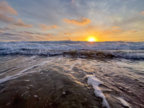 Three distinct waves breaking in succession during a vibrant sunset at Carlsbad State Beach.