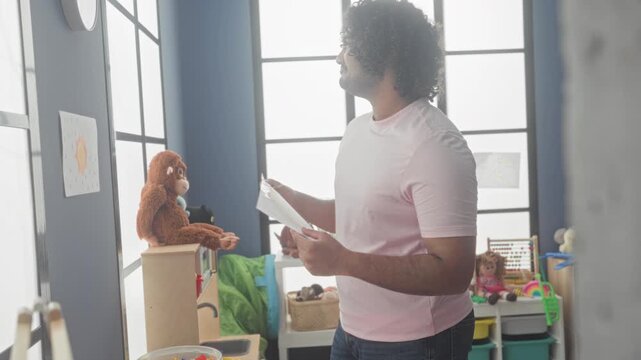 Man pinning child's drawing to classroom wall with hands in kindergarten building; nurturing warmth.