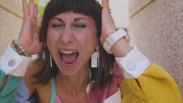 An irritated, angry young Caucasian woman screams in stress and fear, expressing rage and nervousness on the street. A girl on a city street.