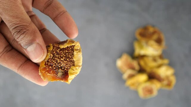 Hand holding dried fig on grey surface with more figs nearby
