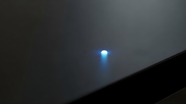 Minimalist blue LED power indicator light on dark metallic surface, glowing electronic status lamp, modern hardware interface detail
