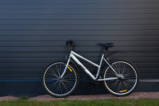 Bicycle parked against a dark wall outdoors, urban transport concept, sustainable commuting, minimal street scene.