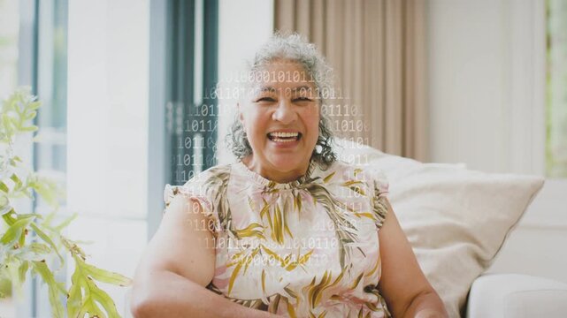 Senior woman speaking on sofa, laughing pointing, causing binary overlay showing tech for creators