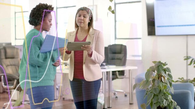 Diverse female coworkers reviewing tablet and holding blue folder in office showing graph overlays