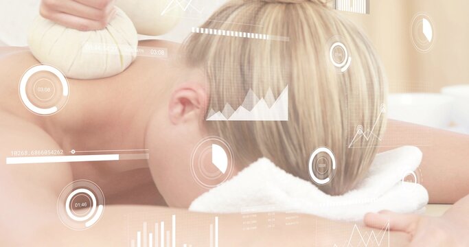 Lying spa client back draped with white towel receiving herbal compress on shoulder, HUD overlays