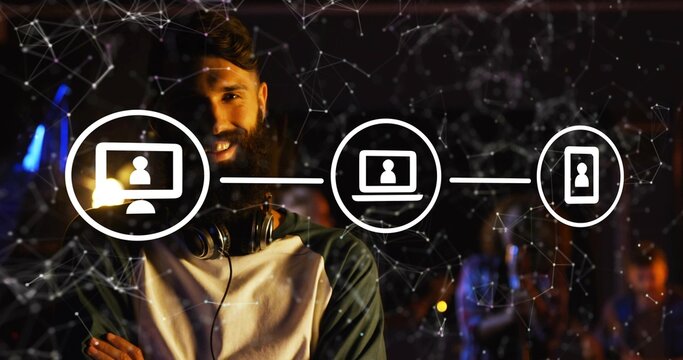 Smiling bearded man standing in dim event venue, wearing raglan tee with headphones, network icons