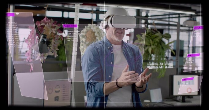 Gesturing mature man wearing denim shirt, white VR headset manipulating AR panels in open office