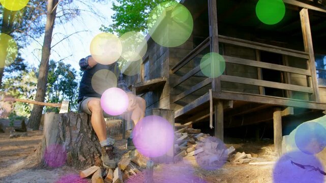 Man drinking bottle on stump after splitting wood, bokeh overlays drifting across man for health