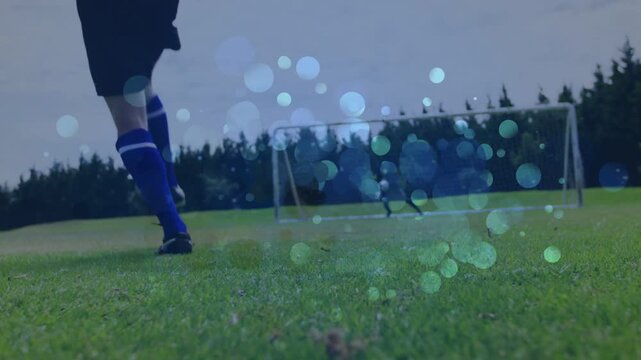 Soccer striker approaching and shooting ball to score, causing goalkeeper diving amid blue bokeh