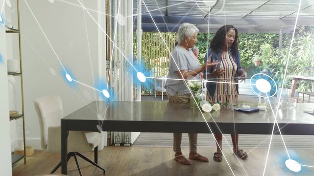 Two women arranging plates while tech nodes expanding and men approaching, finalizing table