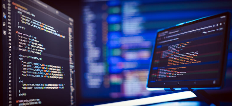 Cyber security concept and hacking. Multiple monitors with complex colorful script syntax in dark mode with shallow depth of field.