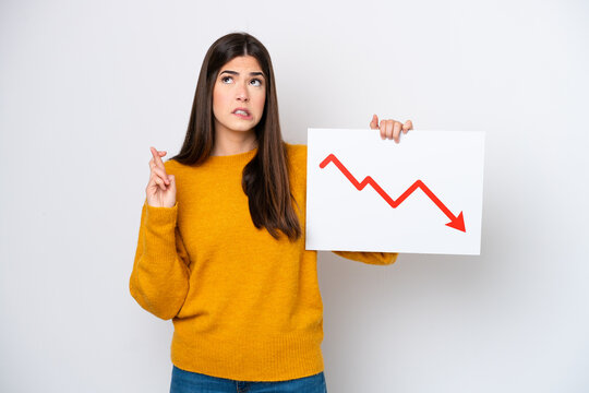 Young Brazilian woman isolated on white background holding a sign with a decreasing statistics arrow symbol with fingers crossing