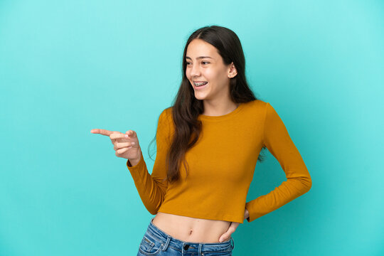 Young French woman isolated on blue background pointing finger to the side and presenting a product