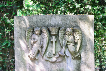zwei Engel in einem Grabstein neben einem Kreuz  auf einem Friedhof in Köln © Blende8