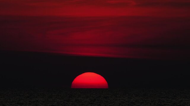 Golden sunset over the sea, captured from a scenic viewpoint. The sun slowly dips below the horizon, casting warm orange and yellow tones. Peaceful and serene atmosphere