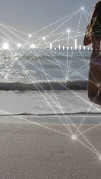 Vertical video: Woman surfer entering right wading into sea with HUD tracking IT data to surf