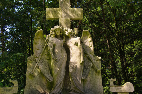 zwei gro&szlig;e sch&ouml;ne Engel vor einem Steinkreuz auf einem Friedhof in K&ouml;ln