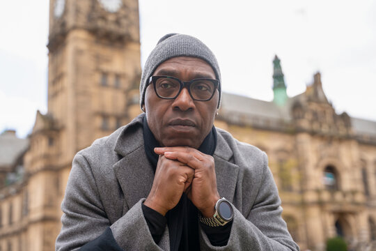 Man in gray coat sits thoughtfully near historical building in city square