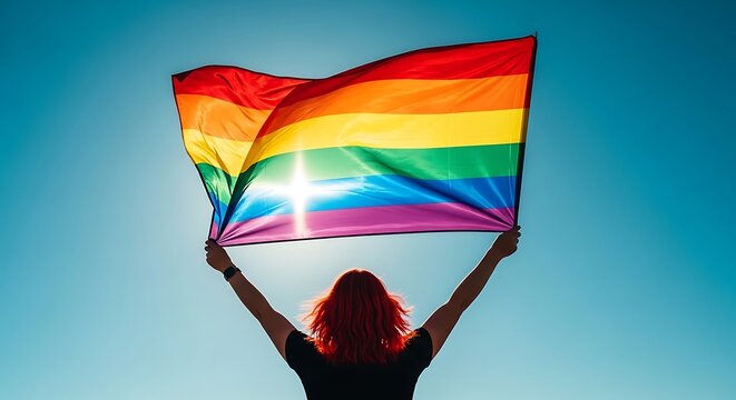 Woman with arms raised holding a rainbow pride flag against the sky, silhouette