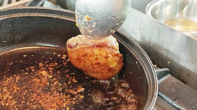 Chef basting seared duck breast with hot oil and juices in a frying pan.