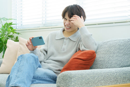 リビングでスマホで動画を視聴する落ち込む日本人男性