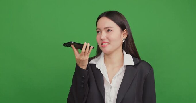 Businesswoman talking into the phone speaker for a voice message on a green screen.