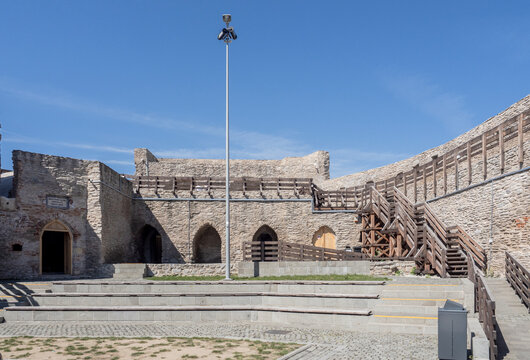 Interior courtyard of the medieval Deva Citadel (Cetatea Devei) in Romania, featuring restored stone walls with arched entrances, wooden walkways, stairs, and a paved amphitheater area