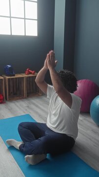 Man on yoga mat, young indian practicing with hands in prayer beside exercise ball and wooden crate in studio; calm focus.