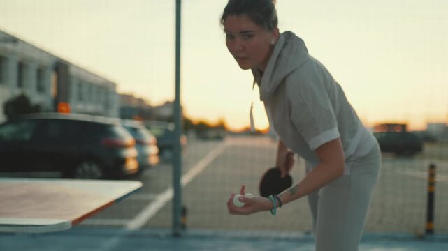 Focused woman playing table tennis outdoors at sunset